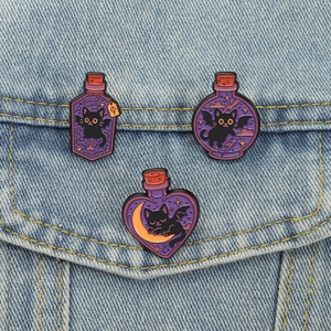 Macro view of three purple enamel cat magic potion pins on light blue denim fabric texture