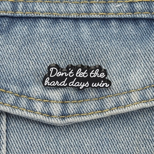 Detail of "Don't let the hard days win" enamel pin on light blue denim jacket