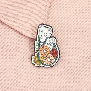 Detailaufnahme einer Emaille-Stethoskop-Brosche mit Blumenmuster auf rosa Stoff