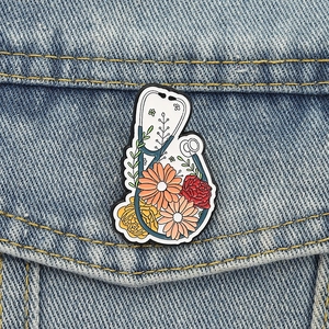 Detail einer floralen Stethoskop-Emaille-Anstecknadel an einer blauen Jeansjacke