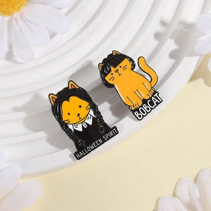 Detail of enamel cat brooches featuring Wednesday Addams and Bobcat designs on a stand
