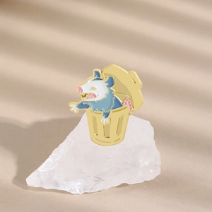 Detalle de un broche de zarigüeya en esmalte en un cubo de basura dorado sobre cristal
