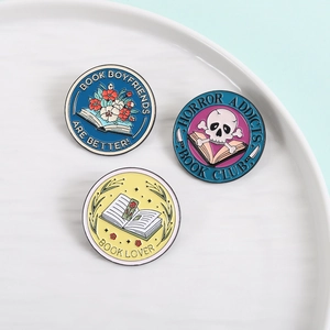 Three round enamel book pins featuring floral motifs, skull motifs, and reader quotes