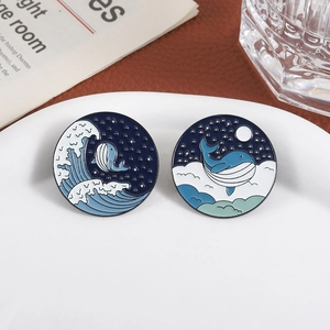 Ocean-themed whale enamel pins set with waves and starry sky patterns on a ceramic tray