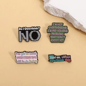 Macro detail of four enamel pins with Overthinking quotes on a neutral stone background