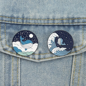 Close-up of whale and ocean themed enamel pins pinned on a light blue denim jacket pocket