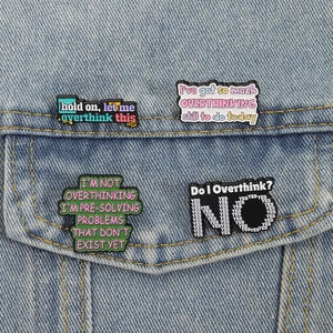 Detailed view of four overthinking-themed enamel pins on a blue denim jacket pocket