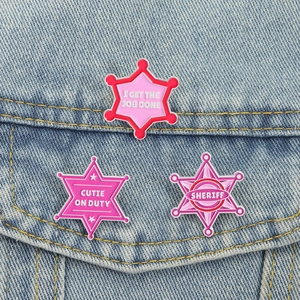 Close-up of pink enamel star badges featuring creative slogans on blue denim jacket pocket