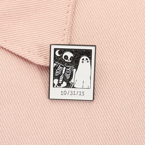Macro shot of Halloween ghost and skeleton polaroid enamel pin on pink fabric