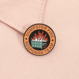 Détail macro du pin's émaillé Dumpster Fire Response Team sur un fond de tissu rose