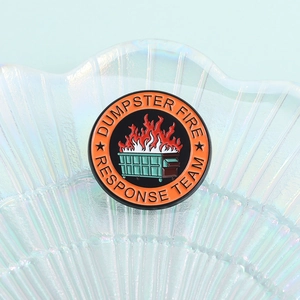 Gros plan du pin's émaillé Dumpster Fire Response Team sur une coupelle en verre