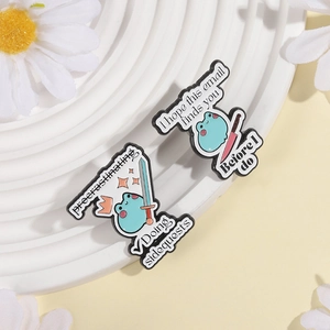 Detail of funny blue frog enamel pins with humorous English text on a white podium