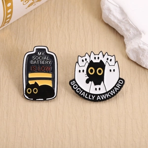 Cute black cat enamel pins with Social Battery and Socially Awkward text on warm background