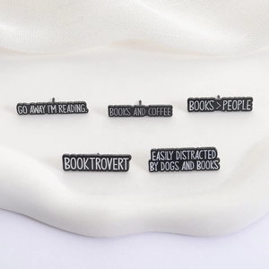 Set of five black enamel pins with book lover quotes displayed on white marble