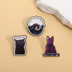 Vue détaillée de trois épingles en émail avec raton laveur Pedro et chat noir sur fond beige