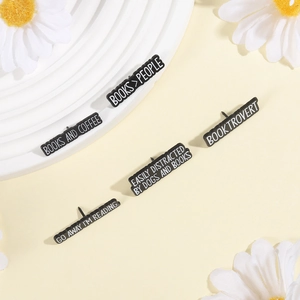 Detail of five black enamel pins with white bookish quotes and metal butterfly clasps
