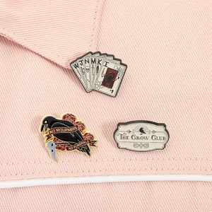 Dettaglio spillette smaltate Six of Crows con logo Crow Club su tessuto rosa fine