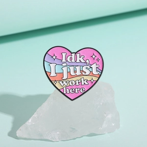 Detail of heart-shaped enamel pin with rainbow stripes and I just work here text