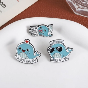 Three cute whale enamel pins set with heart, sunglasses, and flower designs in a white bowl