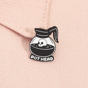 Macro shot of an enamel pothead pin with a skull motif on a textured pink fabric