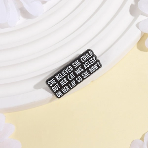 Funny black cat pin with white quote on a white textured tray with flower petals