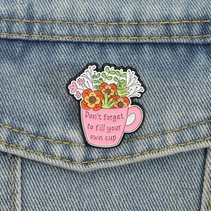 Detail of pink floral cup brooch with 'Don't forget to fill your own cup' quote on denim