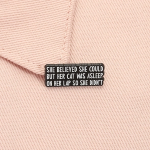 Detail of a rectangular black enamel badge with motivational quote on pink fabric