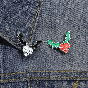 Detail of bat-winged skull enamel pins in black-white and red-green on denim fabric