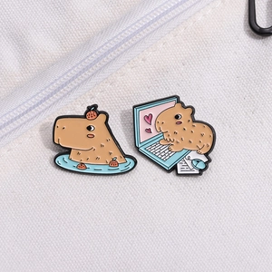Detail of two Capybara enamel pins showing a spa bath and laptop use on white fabric