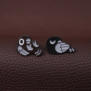 Set of 2 cute black and white punk bird enamel pins displayed on leather background