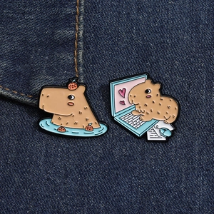 Detail of cute capybara enamel pins with bath and laptop designs on denim fabric