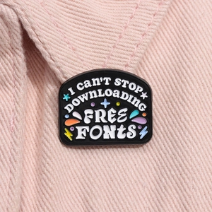 Close-up of a black enamel pin with funny typography on pink denim fabric material