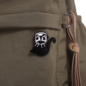 Gros plan d'un pin's chat noir avec casque blanc sur un sac en nylon vert forêt