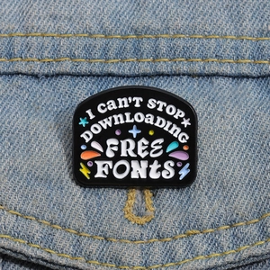 Black enamel brooch with 'I CAN'T STOP DOWNLOADING FREE FONTS' text on denim fabric