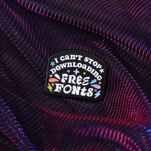 Macro detail of black enamel brooch with I CAN'T STOP DOWNLOADING FREE FONTS text