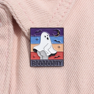 Détail macro du pin's émaillé fantôme d'Halloween avec texte BOOOOOOTY sur du denim