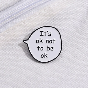 Close-up of enamel pin with 'It's ok not to be ok' quote on white canvas background