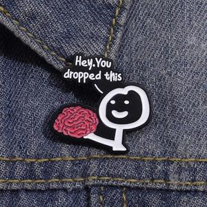 Close-up of funny enamel pin showing cartoon figure holding a pink brain on denim