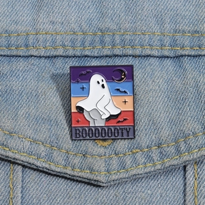 Détail d'un pin's émaillé fantôme rigolo avec texte BOOOOOOTY sur une veste en denim