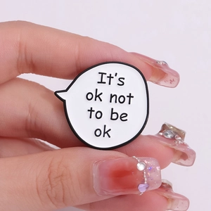 Minimalist 'It's ok not to be ok' speech bubble enamel pin shown held between fingers
