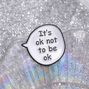 Cartoon speech bubble enamel pin with It's ok not to be ok text in white and black