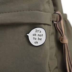 Close-up of enamel pin with 'It's ok not to be ok' text on a green canvas bag