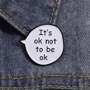Macro shot of an enamel speech bubble pin with 'It's ok not to be ok' on denim fabric