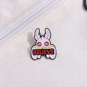 Cartoon white reindeer enamel pin with red BELIEVE lettering on a white fabric background