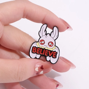 Cartoon moth fairy enamel pin holding a BELIEVE sign with wings and red eyes