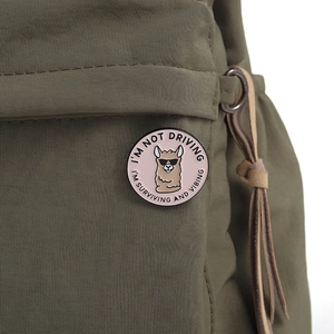 Close-up of a pink alpaca enamel pin with funny quote attached to an olive green canvas bag
