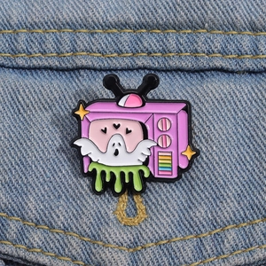 Rosa Retro-TV-Emaille-Anstecknadel mit weißem Geist auf einer blauen Jeansjacke