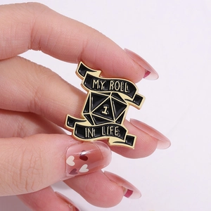 Close-up of MY ROLL IN LIFE black enamel d20 dice pin with gold trim on a scroll