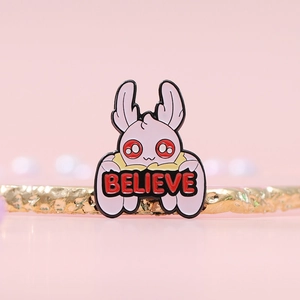 Cartoon pink enamel pin featuring a cute moth-rabbit spirit with BELIEVE text banner
