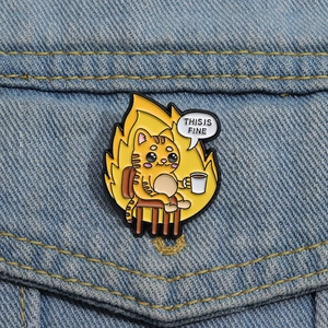 Close-up of This Is Fine cat enamel pin with coffee cup on blue denim fabric background